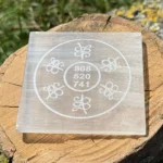 Front-facing image of Grabovoi code engraved Selenite charging plate placed on a wooden surface